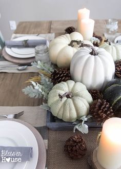 a wooden table topped with white pumpkins and pine cones