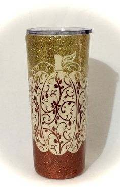 a gold and white pumpkin decorated tumbler with red glitter on the bottom, sitting against a white background