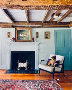 a dog sitting on a chair in front of a fire place with a painting above it