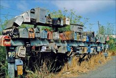 many mailboxes are stacked on top of each other near the side of the road