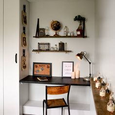 a desk and chair in a room with shelves on the wall above it, along with candles