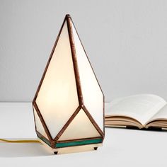 an open book sitting on top of a table next to a lamp that is shaped like a diamond