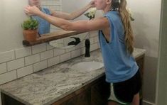 a woman brushing her teeth in front of a bathroom mirror with a potted plant on the counter