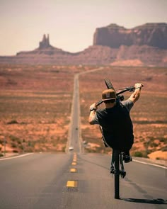 a man riding a bike down the middle of a road with mountains in the background