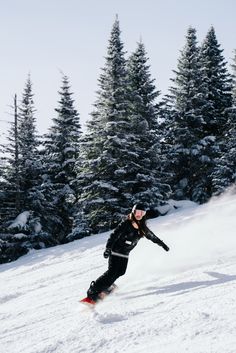 a person riding a snowboard down the side of a snow covered slope with trees in the background