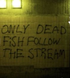 graffiti written on the side of a brick wall in a subway station reads, only dead fish follow the stream