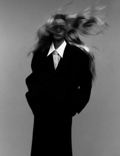 a woman with her hair blowing in the wind wearing a black coat and white shirt