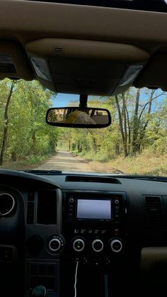 the view from inside a car looking at a dirt road with trees on both sides