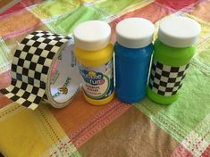 three different colored bottles sitting on top of a bed next to a checkered table cloth