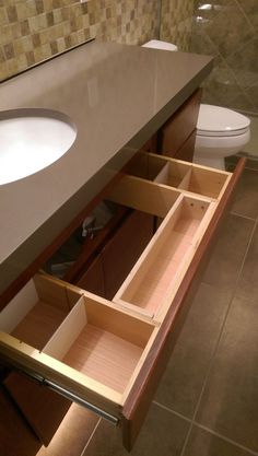 an open drawer in the middle of a bathroom counter next to a toilet and sink