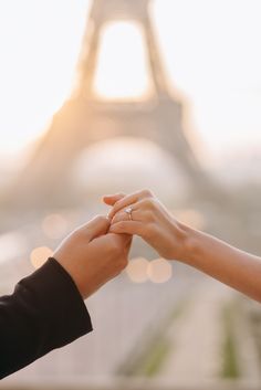 two people holding hands in front of the eiffel tower