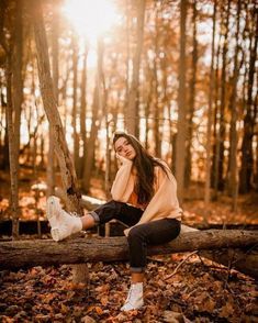 a woman sitting on a log in the woods with her legs crossed and smiling at the camera