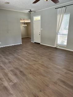 an empty living room with hard wood flooring and ceiling fan in the center area