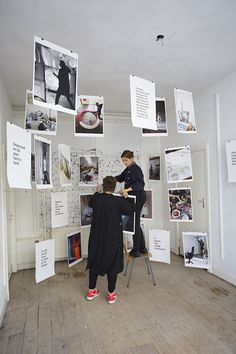 two people standing in front of a wall with pictures hanging from it and on the walls