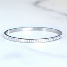 An elegant row of rhinestones sparkle on this stainless steel bracelet. Designed to stack with our Goldenerre watch bands, this waterproof, stainless steel bracelet will not rust or tarnish. Its oval shape is feminine and flattering, elegant when worn alone or "extra" when stacked with our stainless steel bracelets. Stainless steel with gold or silver plating. Will not rust or tarnish. Waterproof Available in two sizes: Small fits up to 6.5" wrist, Medium up to 7.5" wrist Hinged opening Imported Stainless Steel Jewelry With Diamond Accents, Anniversary Jewelry With Stainless Steel Clasp, Timeless Stainless Steel Bracelets For Anniversary, Luxury Stainless Steel Jewelry With Rhinestones, Elegant Stainless Steel Bracelets With Bling, Elegant Stainless Steel Bracelets With Diamond Accents, Elegant Jewelry With Stainless Steel Clasp For Anniversary, Elegant Stainless Steel Bling Bracelets, Elegant Anniversary Jewelry With Stainless Steel Clasp