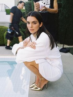 a woman sitting on the ground in front of a pool wearing gold shoes and a white robe