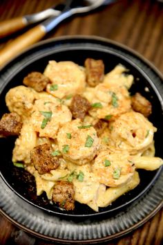 a black plate topped with pasta and meat covered in cheese sauce on top of a wooden table