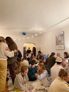 a group of people sitting and standing around each other in a room with white walls