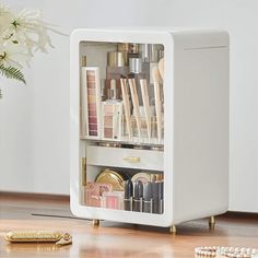 a white cabinet filled with lots of cosmetics and other items on top of a wooden floor