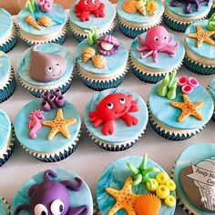 cupcakes decorated with sea animals and seashells are displayed on a table