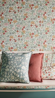 three pillows on a bench in front of a wallpapered wall with flowers and leaves