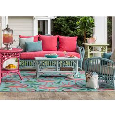 an outdoor living room with colorful furniture and pillows on the couch, coffee table, and rug