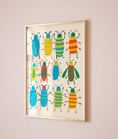 an insect print hangs on the wall next to a white framed painting with four different colored bugs