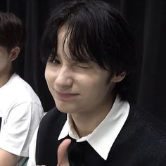 two young men sitting next to each other in front of a black curtain and giving the thumbs up sign