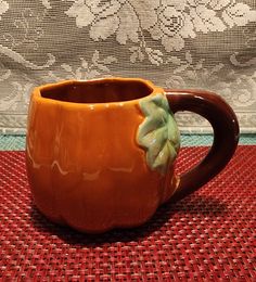 a ceramic coffee mug with a green flower on the handle sits on a red tablecloth