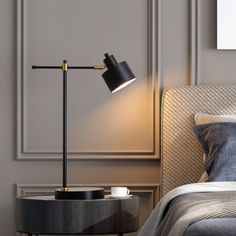 a bed with a black lamp on top of it next to a night stand and side table