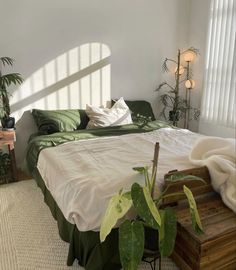 a bedroom with white walls, green bedding and potted plants in the corner