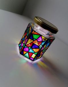 a glass jar filled with colorful lights on top of a white table next to a wall