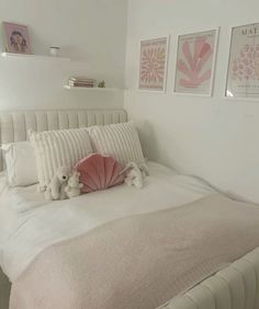 a white bed topped with pillows and stuffed animals next to two pictures on the wall