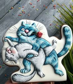 a hand holding a cookie with a cat and kitten on it's back, in front of some sprinkles