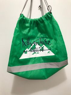 a green bag hanging on a wall with the words adventure awaits written on it