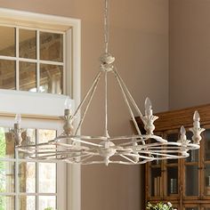 a chandelier hanging from the ceiling in a dining room with windows and potted plants