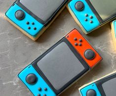 four decorated cookies shaped like nintendo wii gameboys on a gray surface with blue and orange frosting