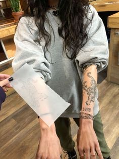 a woman with long hair and tattoos on her arm holding up a piece of paper