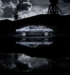 a black and white photo of a car in front of a crane on a cloudy day