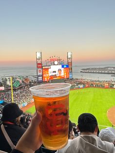 a person holding up a beer at a baseball game