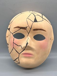 a white mask with cracked paint on it's face is shown in front of a gray background