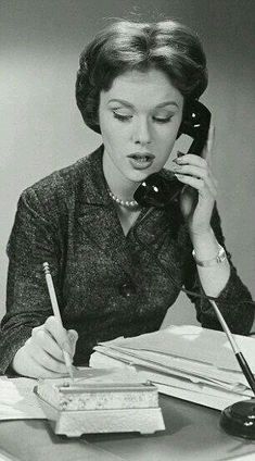 a woman sitting at a desk talking on the phone while holding a pen and paper