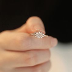 a woman's hand holding an engagement ring with three stones on it and the middle finger