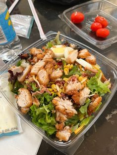 a salad in a plastic container on a table with some tomatoes and other food items