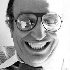 a black and white photo of a man with glasses on his face smiling at the camera