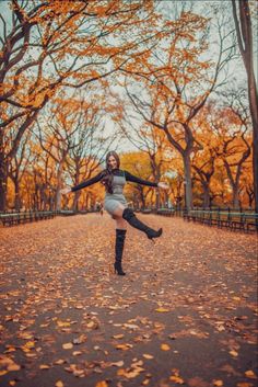 a woman is dancing in the middle of an autumn park