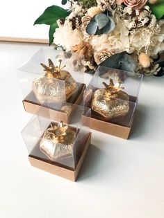 there are four small boxes with gold decorations on top of each box and flowers in the background