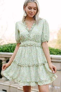 This one-of-a-kind sage green floral mini dress is the perfect piece to make you stand out! Featuring a flattering ruffle hem and a feminine midi length, you'll be sure to turn heads in this show stopping look. This dress features a cut out back, short puff sleeves, a v-neck, ruffled detailing, and a tiered skirt.  Material has no amount of stretch.Cam is wearing the small. Sage Green Floral, Floral Cocktail Dress, Black Tie Dress, Long Sleeve Outerwear, Two Piece Swimwear, Out Back, Floral Print Blouses, Romper With Skirt, Spring Outfits Casual