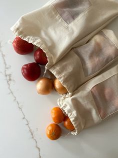 three bags with apples and oranges in them on a white counter top next to other fruit