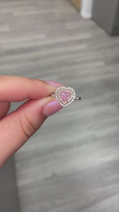 a woman's hand holding a pink heart shaped diamond ring in her left hand